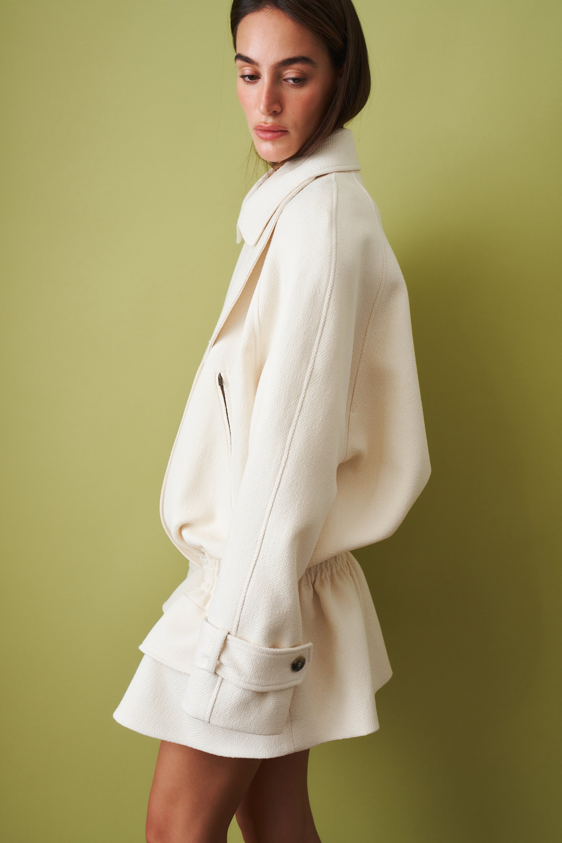 Ecru coat by THE MANNEI, stylish jacket with a tailored fit, shown on a hanger against a neutral background.