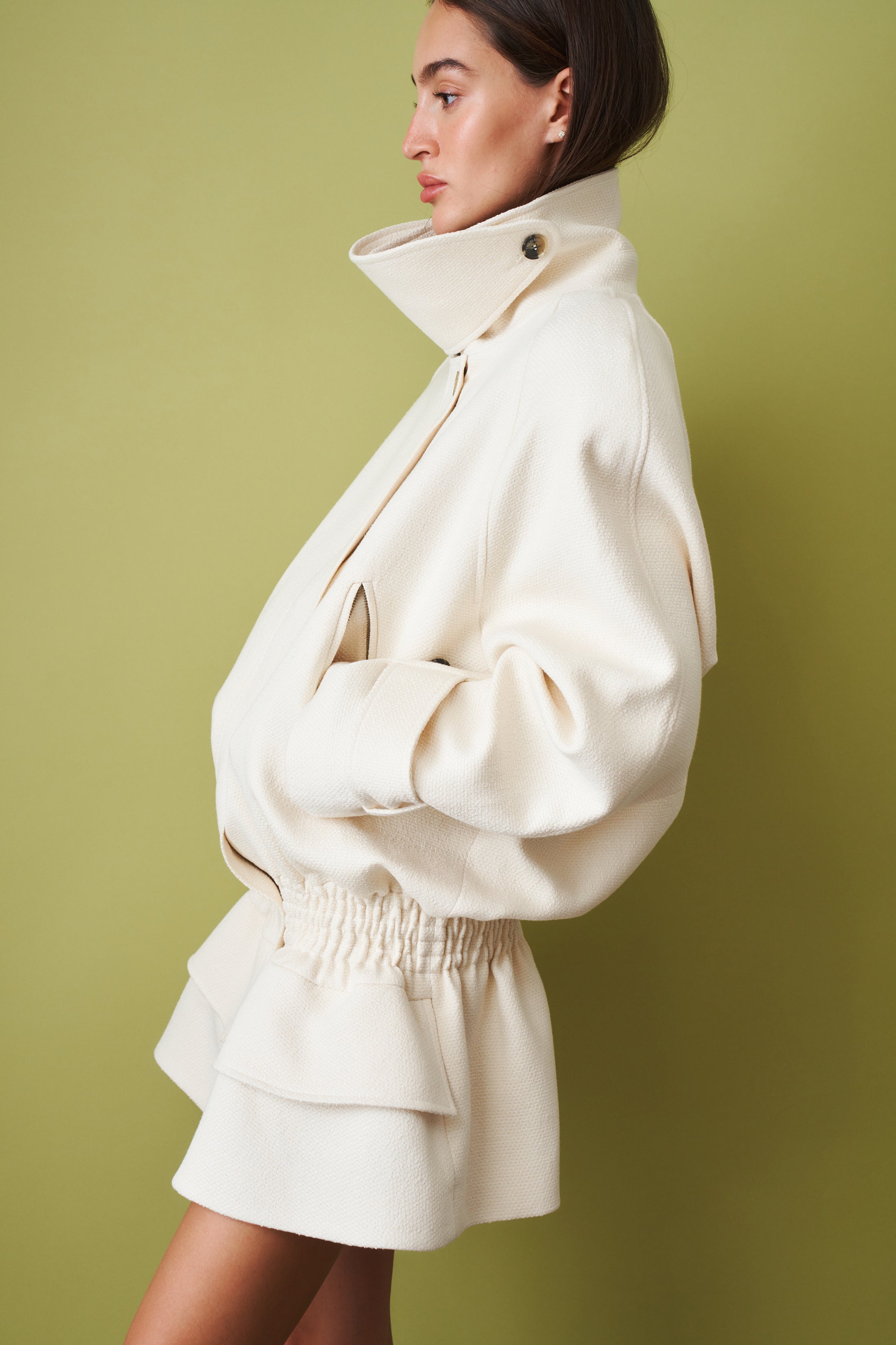 Ecru coat by THE MANNEI, stylish jacket with classic design and textured fabric, displayed on a hanger.