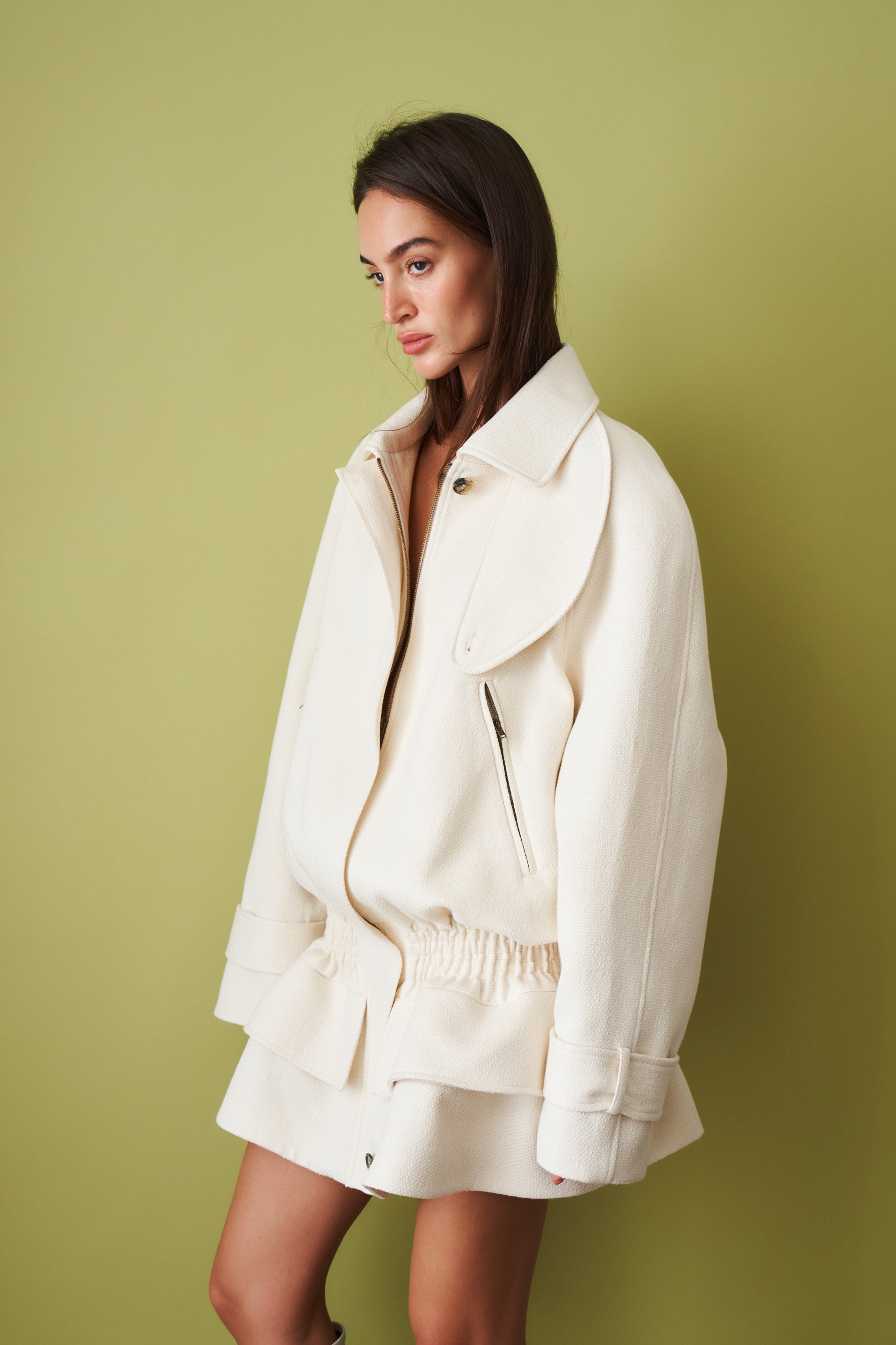 Ecru coat by THE MANNEI featuring a stylish jacket with a classic design and textured fabric, displayed on a hanger.