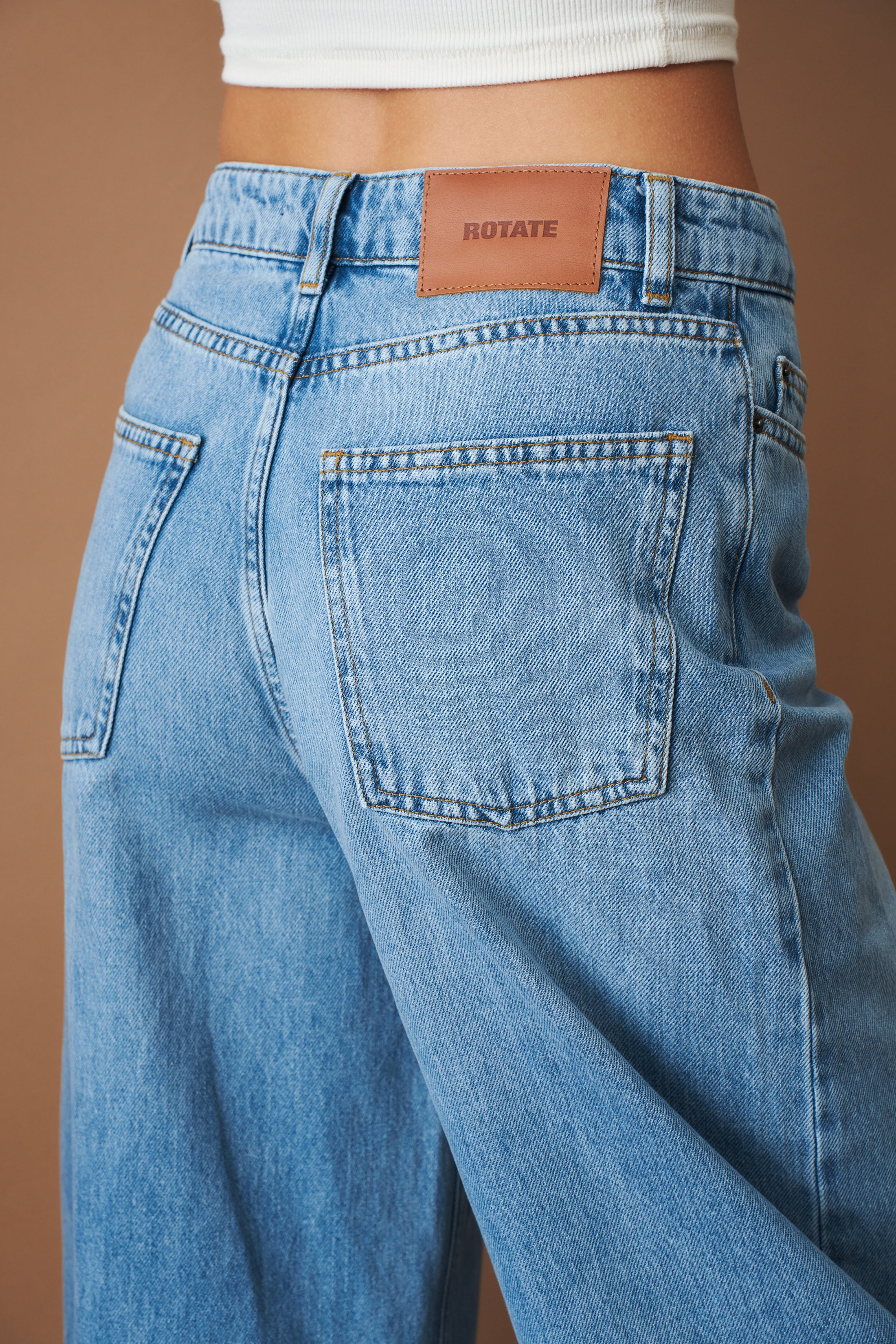 Rotate Draped Barrel Leg Jeans, stylish pants with a relaxed fit and unique draped design, shown in a fashion photoshoot image.